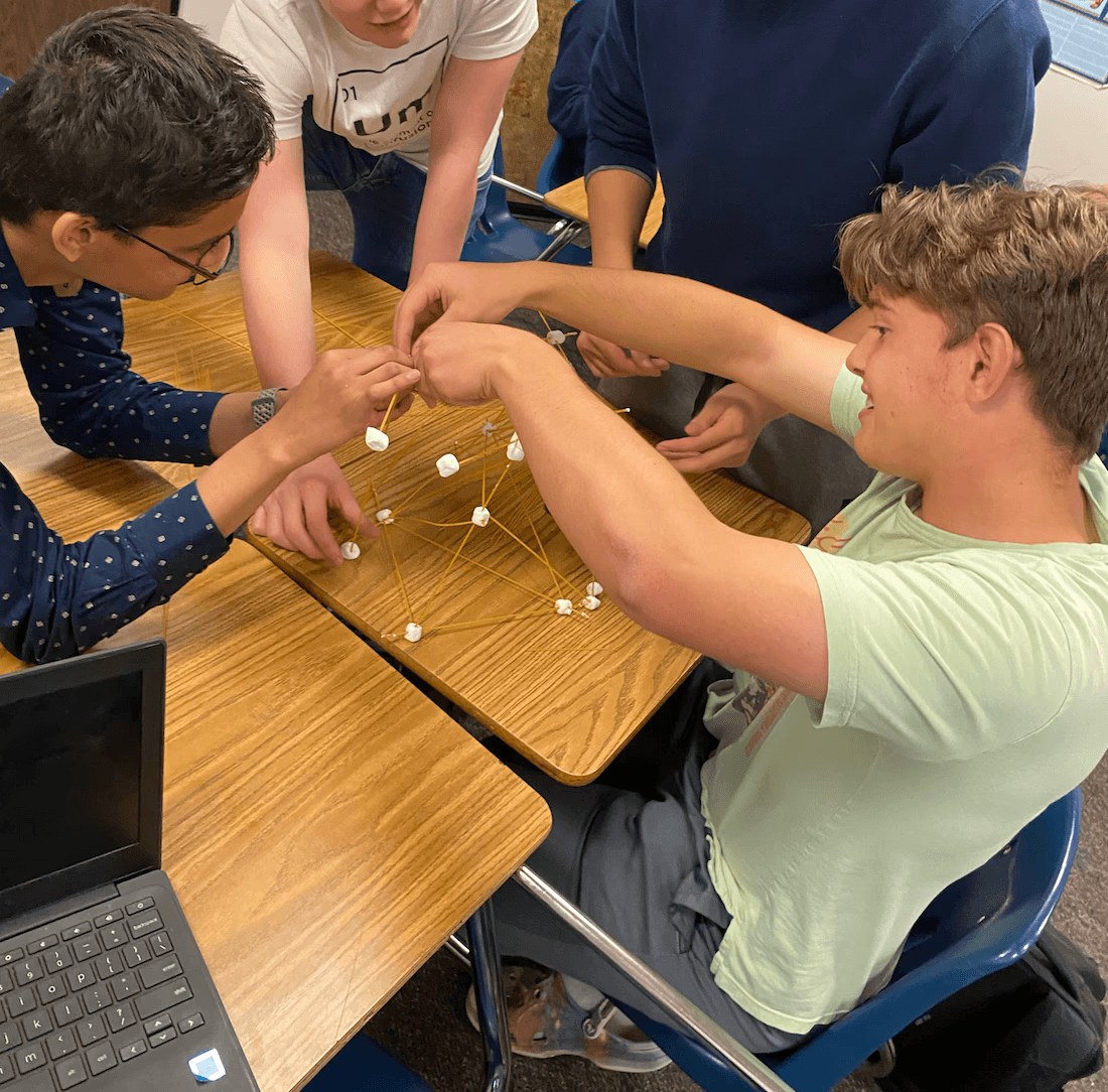 Students building a structure out of marshmallows and toothpicks at a classroom desk